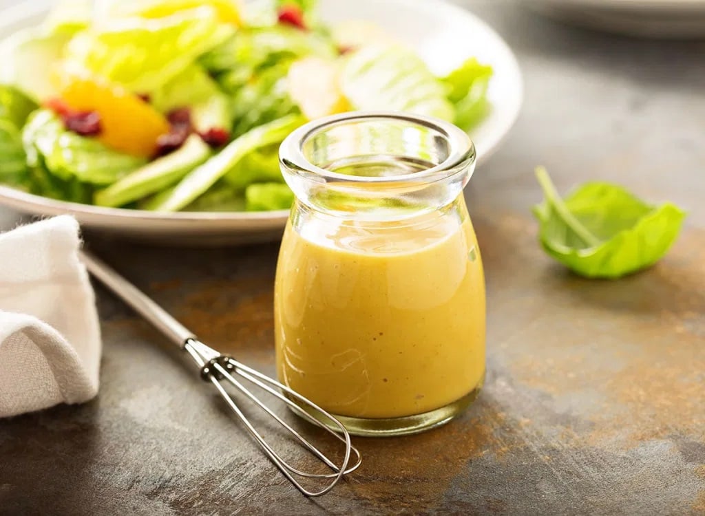 Salad dressing made with canola oil beside a plate of fresh salad