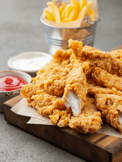 Fried chicken and fries on a wooden board next to cups of ketchup and aioli