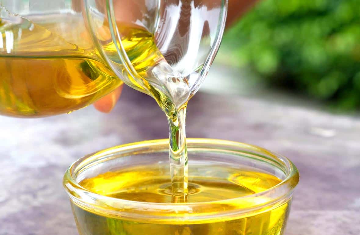 A hand pouring oil into a bowl on the kitchen table