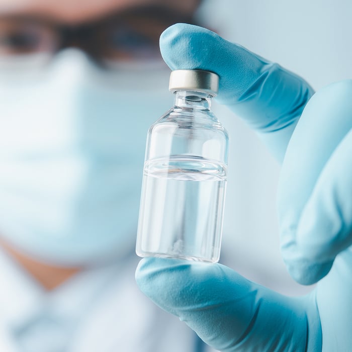 A close up of a gloved hand holding a bottle of medicine