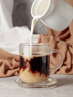 Creamer being poured into a cup of coffee
