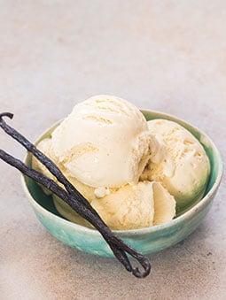 A bowl of vanilla ice cream next to vanilla beans