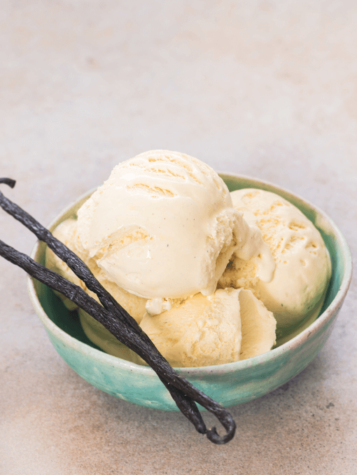 A bowl of vanilla ice cream next to vanilla beans