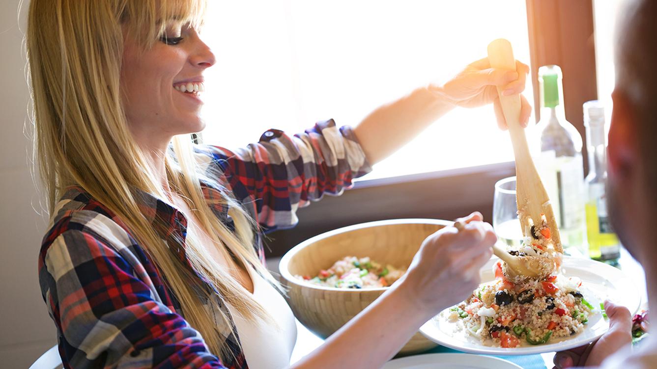 A person serving an ancient grains and vegetable salad onto a plate