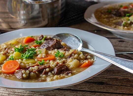A white bowl with a stew containing ancient grains, carrots, beef, and potatoes