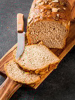 A loaf of whole grain bread with seeds and a few slices cut