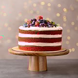 A red and white layered cake topped with berries on a wooden cake stand