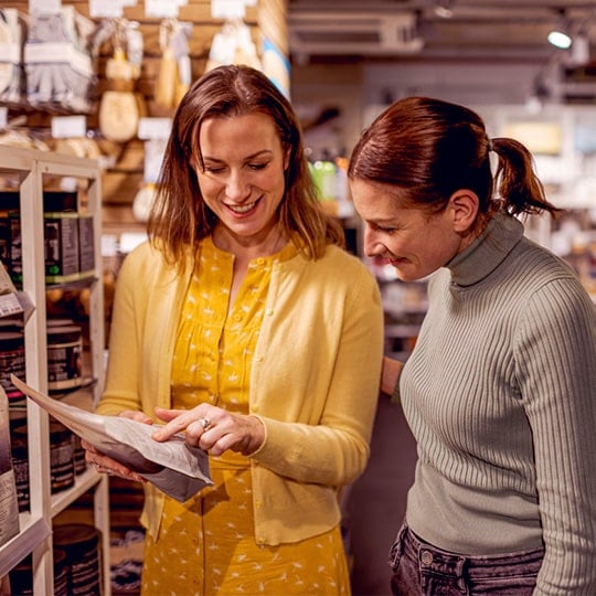 Two women in grocery aisle reviewing product ingredients