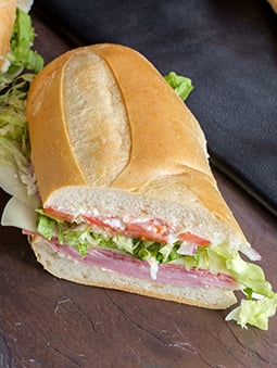 A hoagie-style sandwich with white bread, meats, lettuce, tomato, and mayonnaise