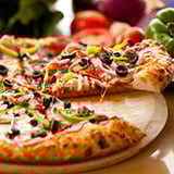 A supreme pizza with black olives, green peppers, and sausage with a slice being lifted from the rest of the pizza