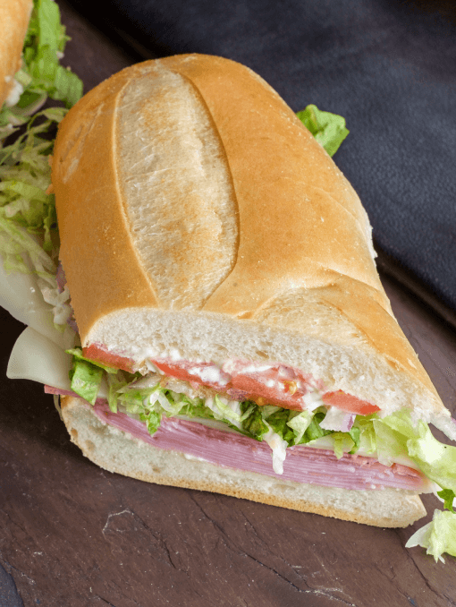 A hoagie-style sandwich with white bread, meats, lettuce, tomato, and mayonnaise
