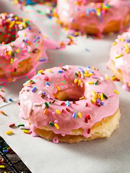 A donut covered in light pink icing and multicolored sprinkles