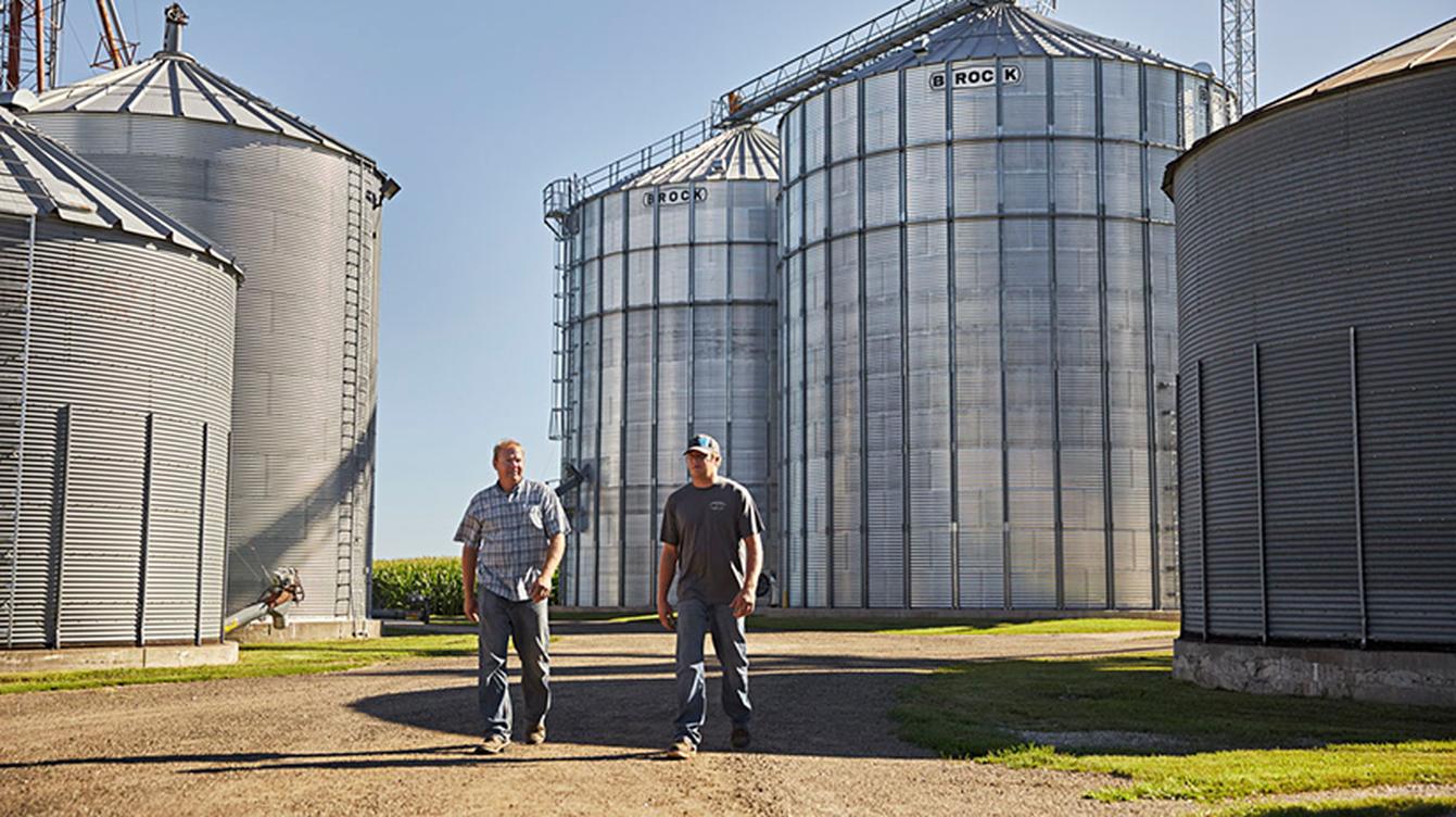 Two people standing outside next to several grain silos