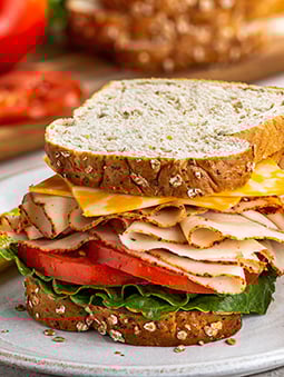 A sandwich on organic flour oat bread with cheese, deli turkey, tomatoes, and lettuce