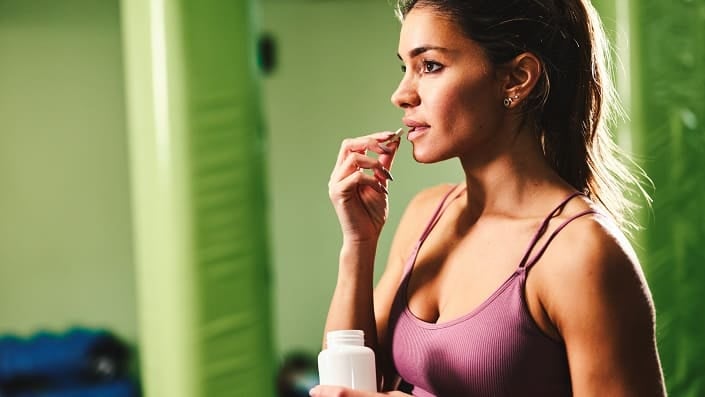 A woman in gym clothes eats dietary supplements on a green background