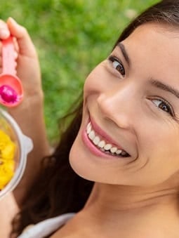 A woman smiles while eating postbiotics products on a grass field