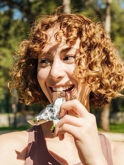 A woman in gym clothes eats a healthy granola bar