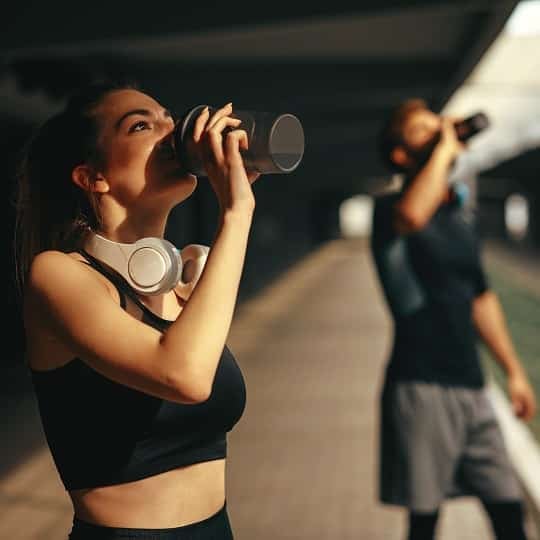 Two people drink a dietary supplement beverage while wearing gym clothes