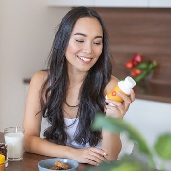 A woman smiles while looking at a box of dietary supplements