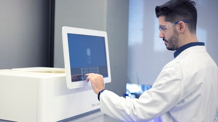 A scientist in a white coat analyses samples on a computer screen