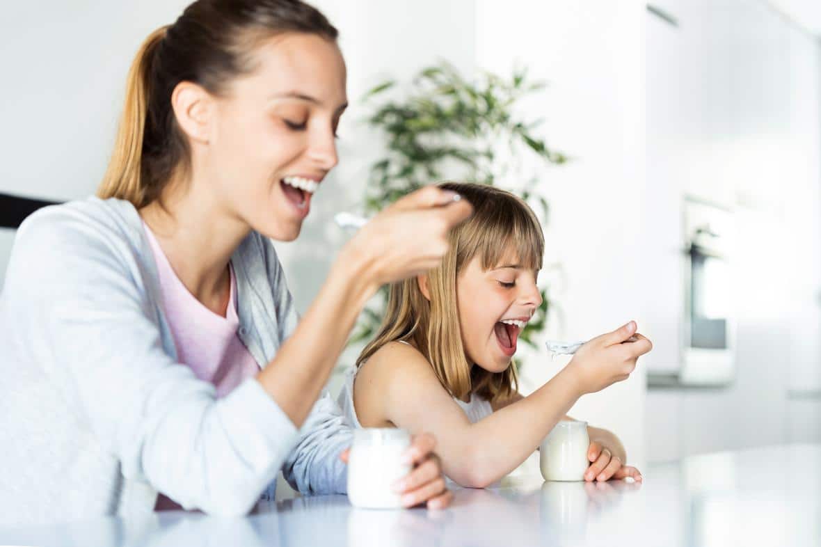 Woman with her daughter eating yogurt at home