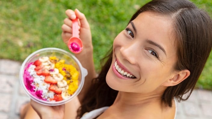 A woman is eating from a colorful bowl and smiling