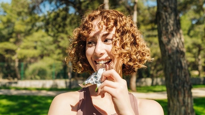 A woman eats a snack bar in a green garden