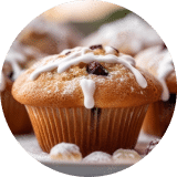 A close-up of a single blueberry muffin covered in powdered sugar and a light drizzle of icing among a tray of the muffins.