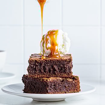 A stack of brownies with a scoop of ice cream atop and caramel being drizzled over