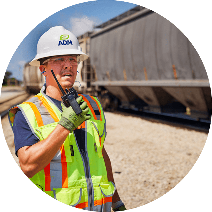 An ADM employee in a white hard hat and reflective safety vest talking into a walkie-talkie