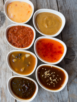 Top-down view of multiple white bowls with a variety of red, orange, and brown sauces 