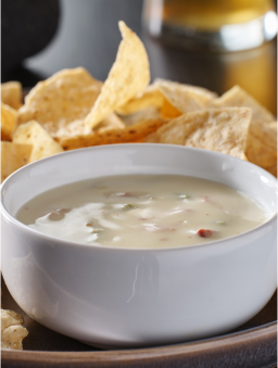 A white bowl of queso blanco on a plate with tortilla chips