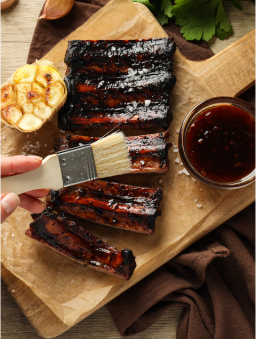 A person’s hand is shown brushing a dark brown marinade onto ribs