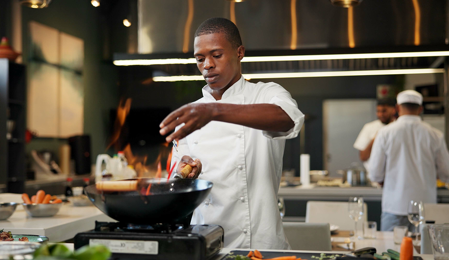 A chef in a commercial kitchen adds spices to a wok