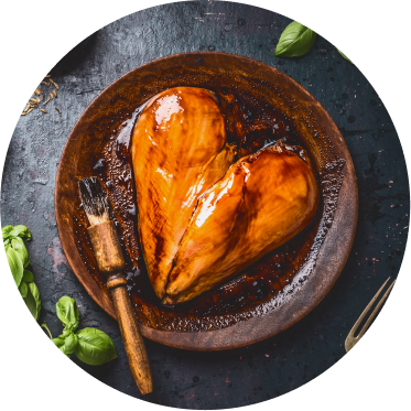 Two chicken breasts basted with a barbecue sauce are placed in a wooden bowl to form a heart