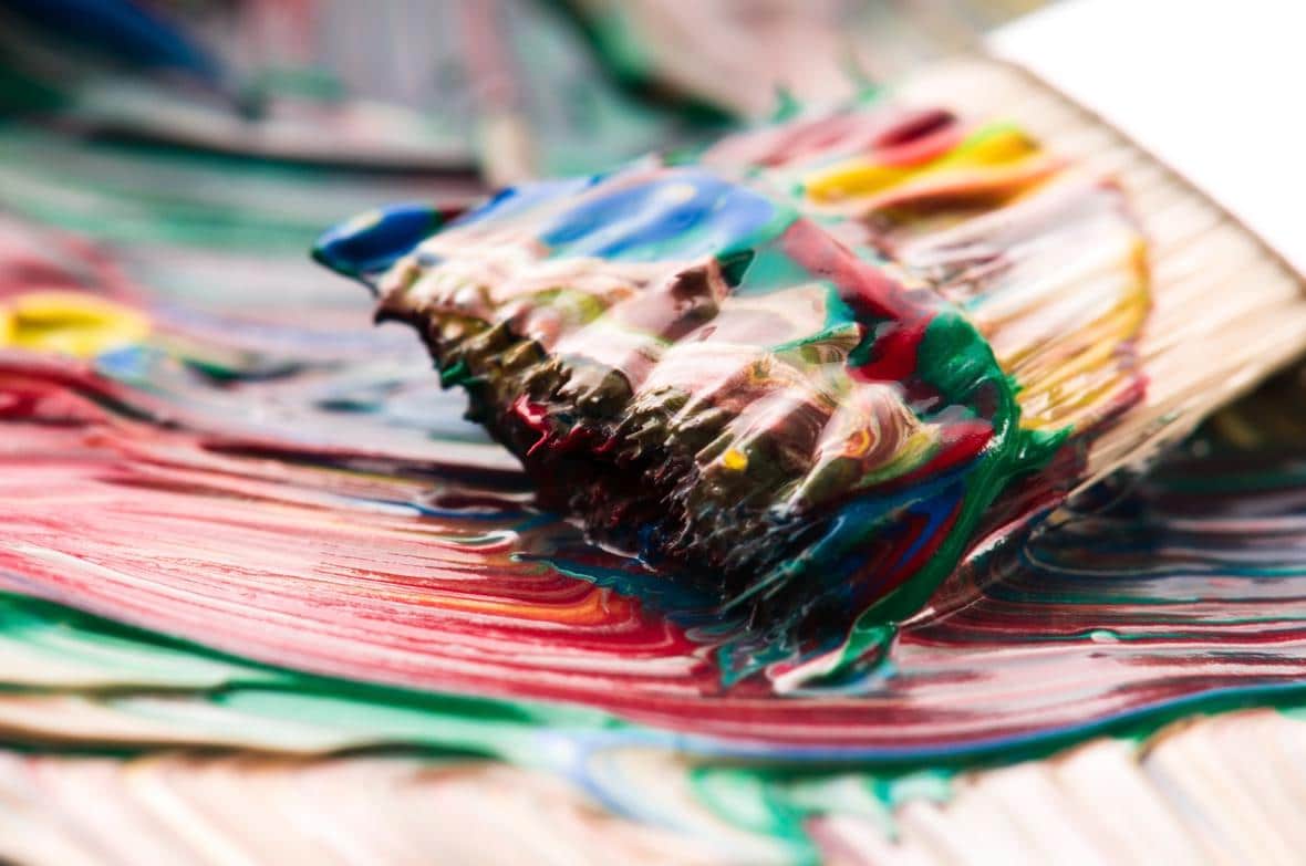A paintbrush mixing paint on a palette
