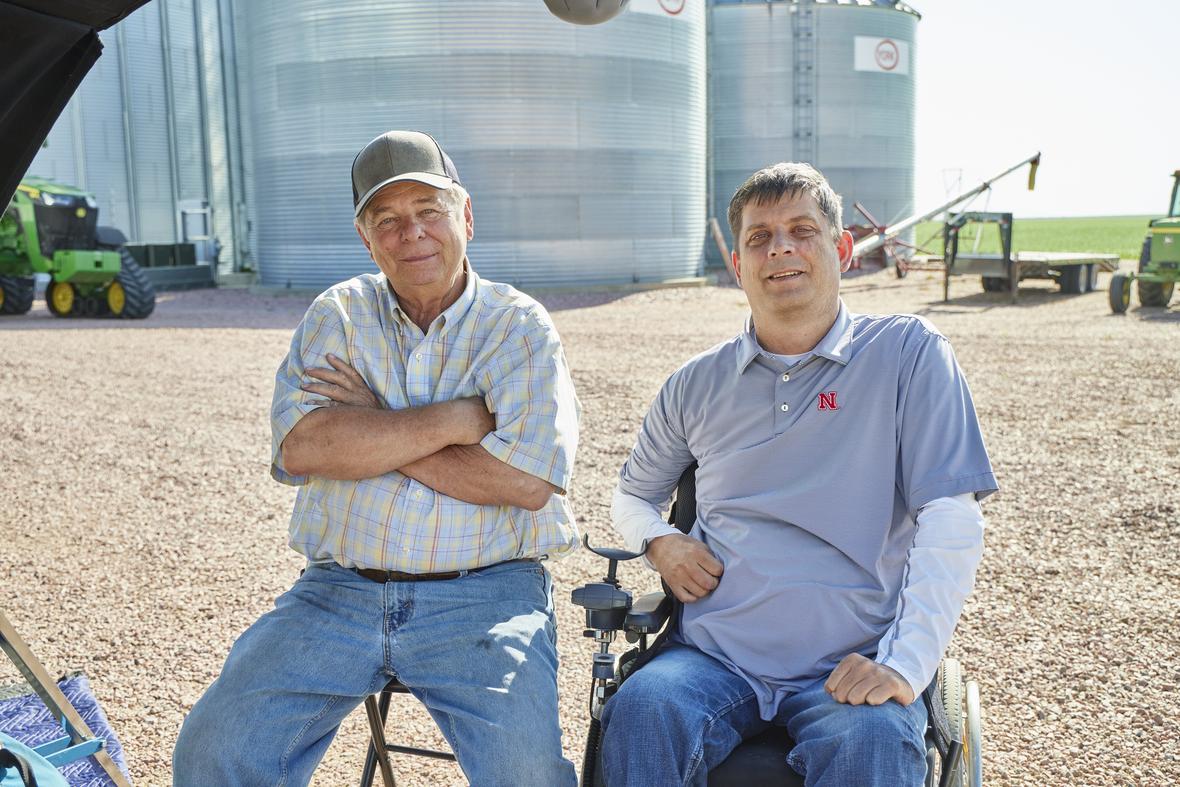 Two farmers are proudly sitting in their corn field and looking at the camera