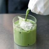 An iced matcha latte being poured into a glass 