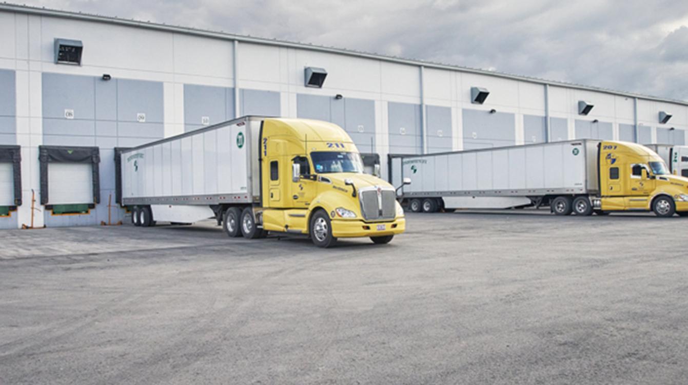 A semi-truck with a yellow cab and white trailer parked at a loading dock