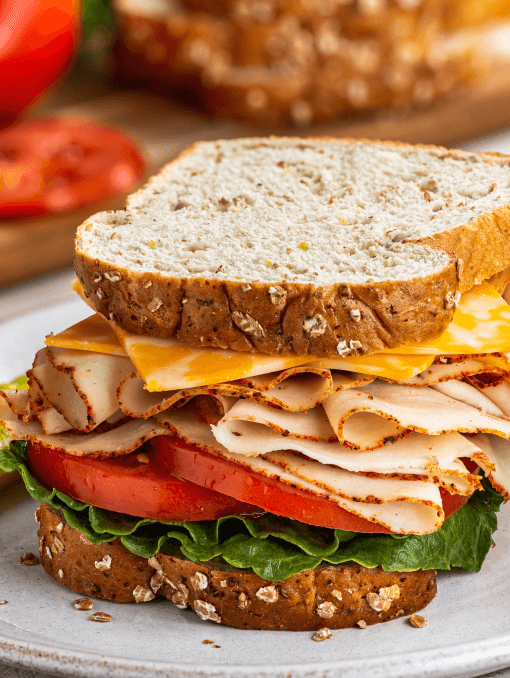 A sandwich on organic flour oat bread with cheese, deli turkey, tomatoes, and lettuce