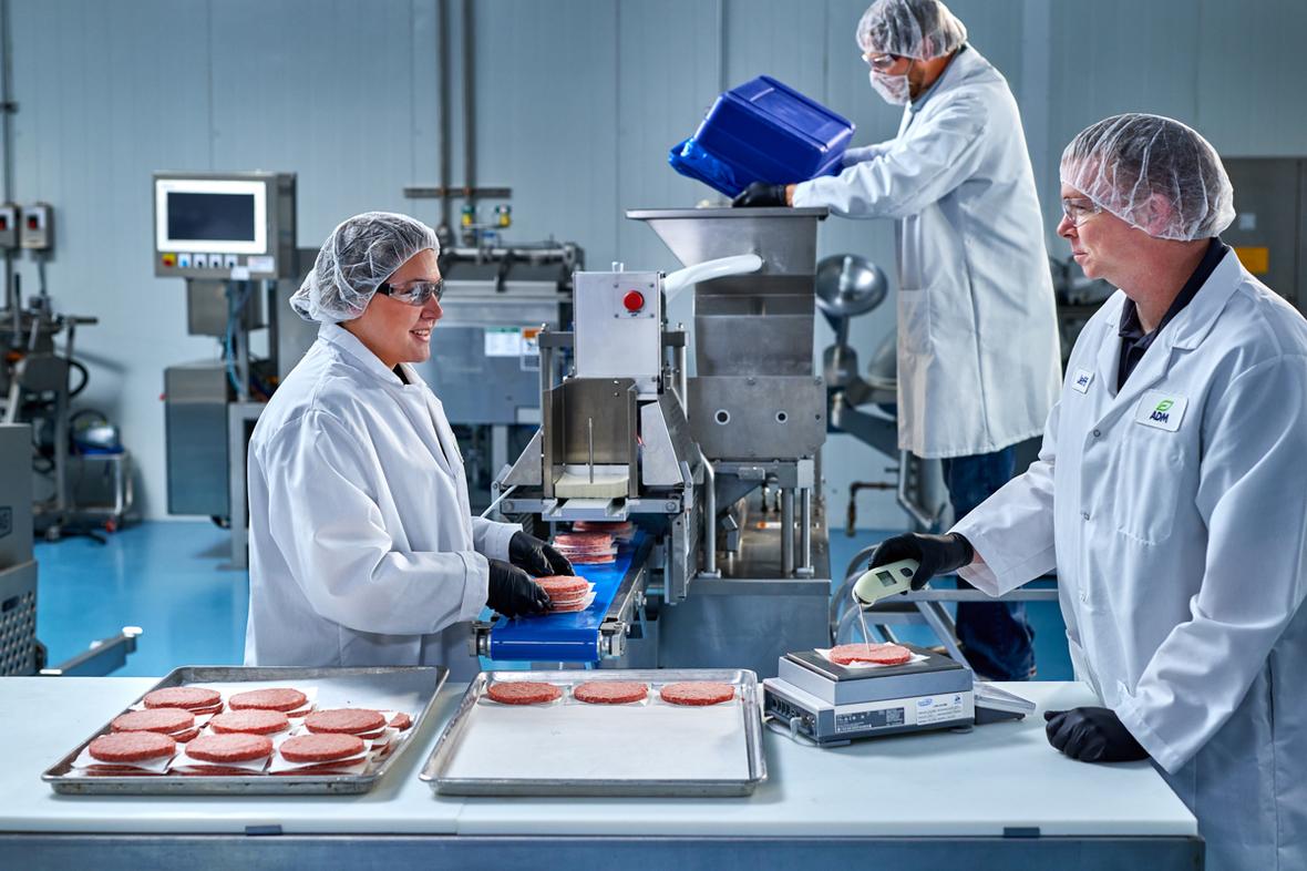 Group of 3 scientists wearing safety gear manufacturing meat.
