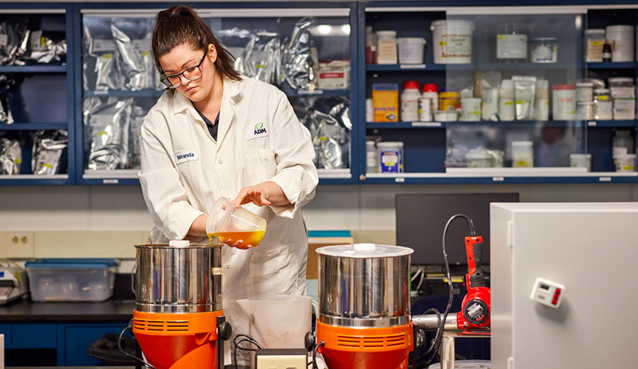 A scientist in a lab setting pouring liquid into a metal container