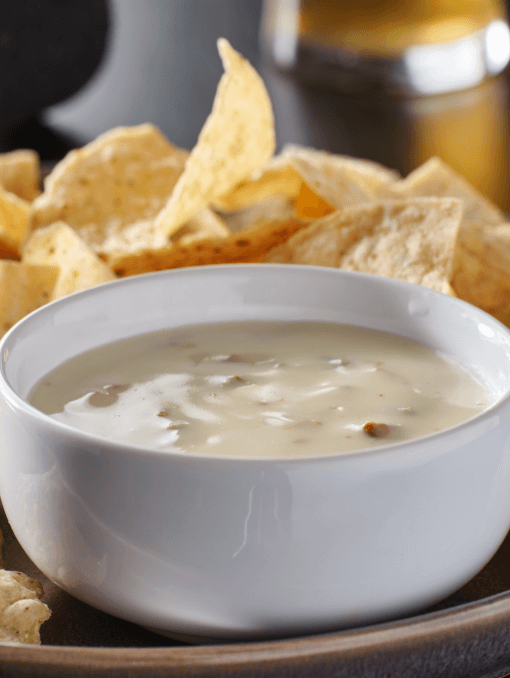 A white bowl of queso blanco on a plate with tortilla chips