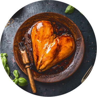 Two chicken breasts basted with a barbecue sauce are placed in a wooden bowl to form a heart