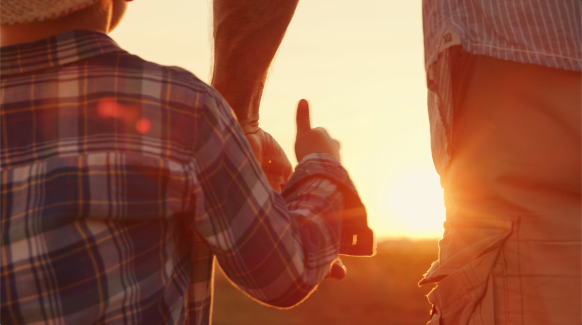 Farmer holding hand of his kid in a wheat field at sunset
