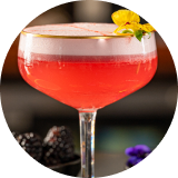 A pink cocktail in a coupe glass and garnished with a yellow pansy