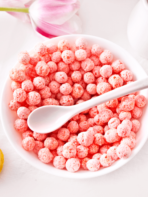 A white bowl of strawberry corn ball cereal made with a naturally derived light pink color