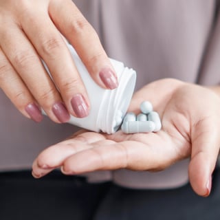 A person holding a pill bottle and shaking out pills into one hand