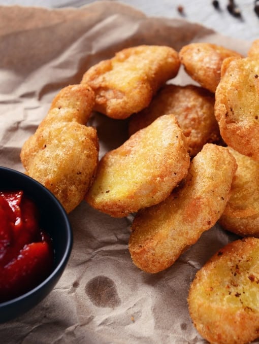 Plant-based chicken nuggets next to a small bowl of red dipping sauce