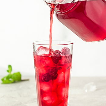 A glass of iced hibiscus tea with raspberries